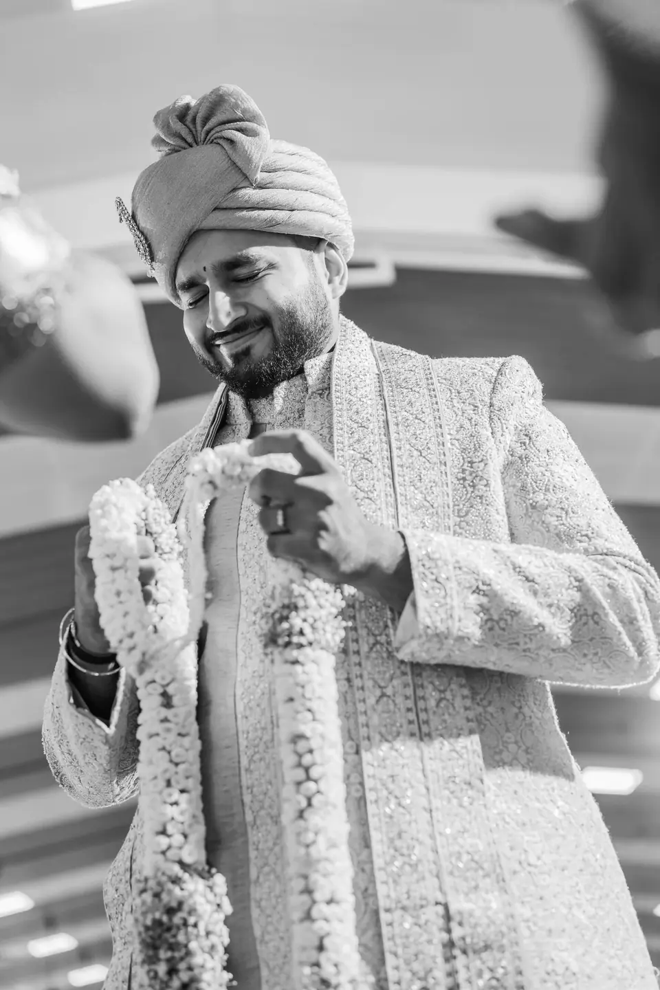 Black and white: the groom looking down at the jasmine garland around his neck