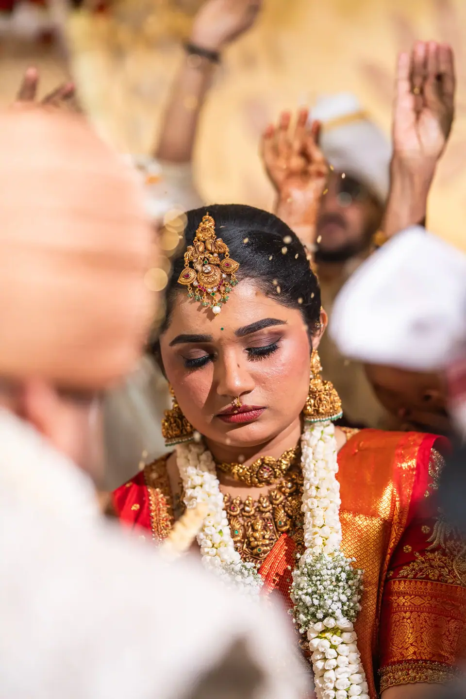 The bride with eyes closed during the rites, jasmine and gold at her neck