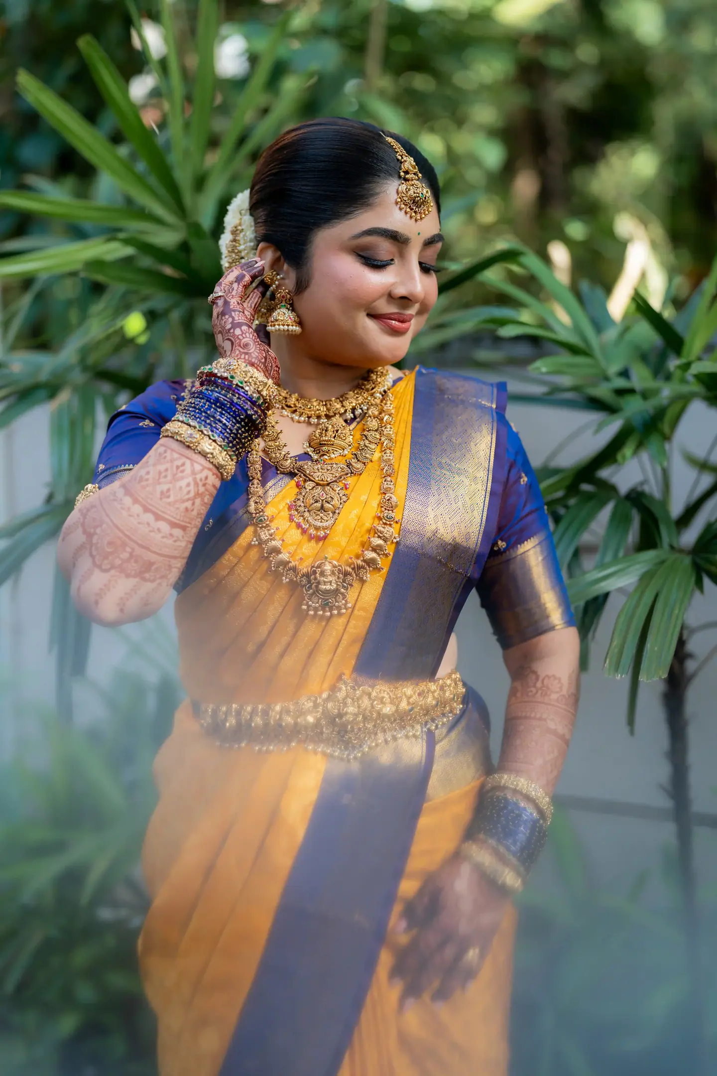 The bride in yellow silk touching her earring among garden leaves