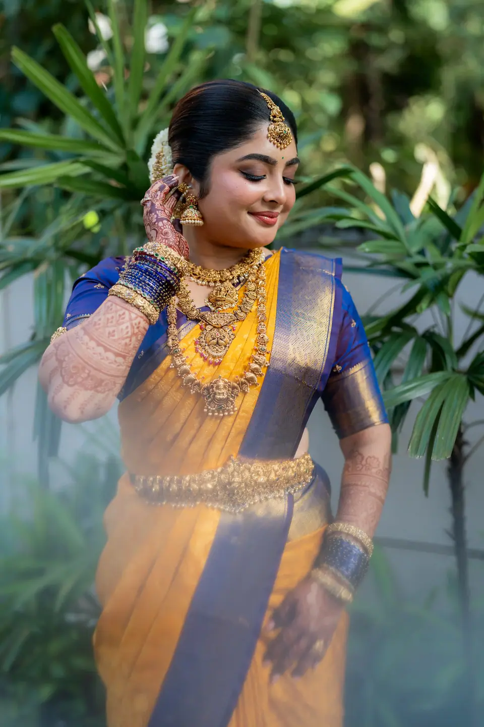 Bride in yellow silk touching her earring among garden leaves