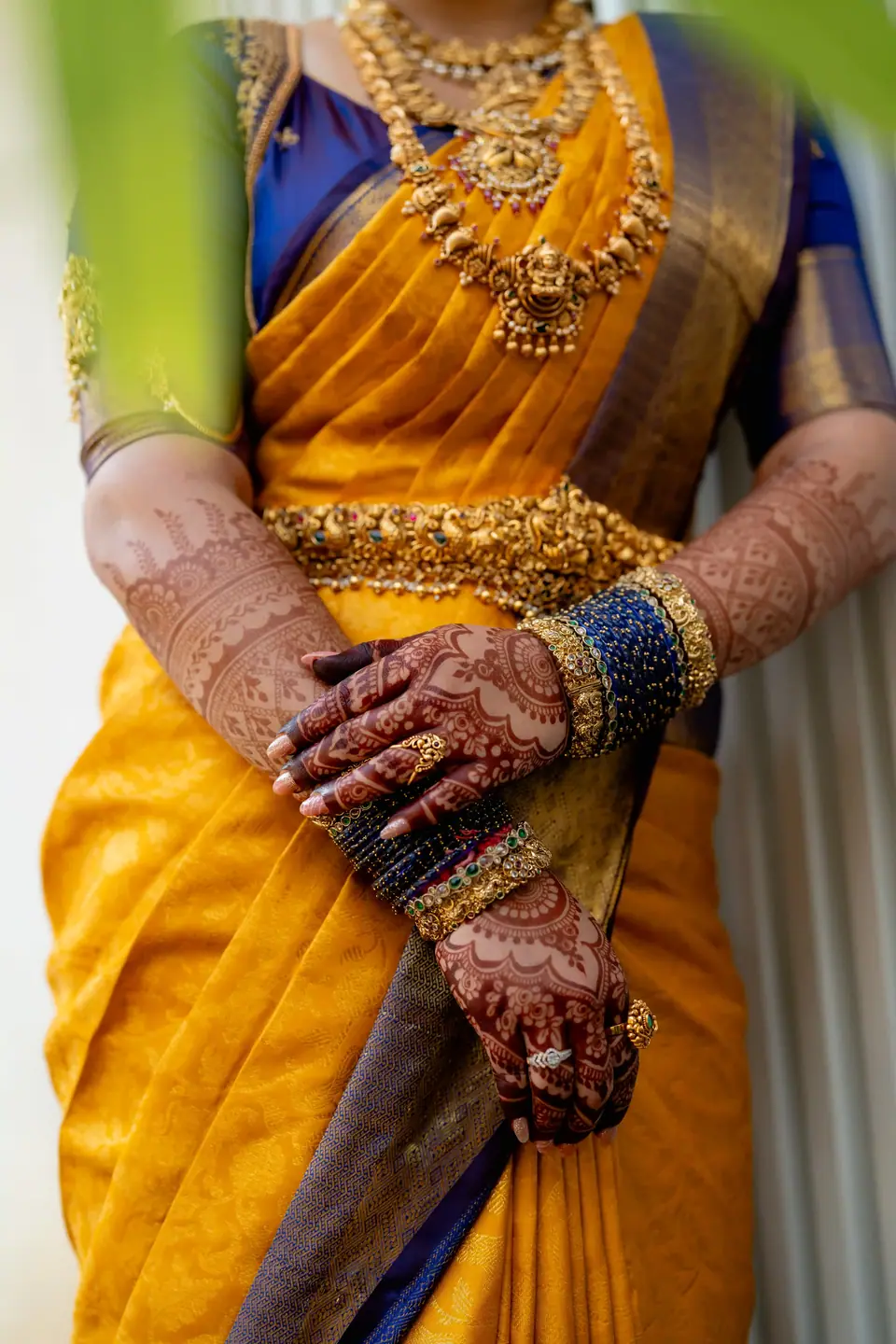 Detail of hennaed hands and gold bangles resting on yellow silk