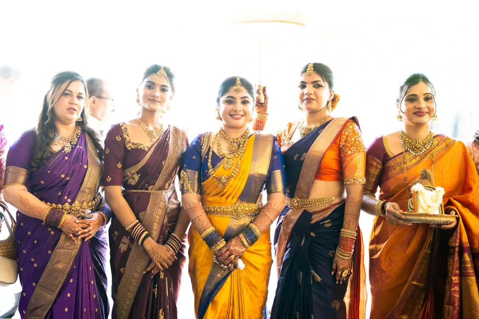 Five women in bright silk sarees laughing as they wait in the sunlight