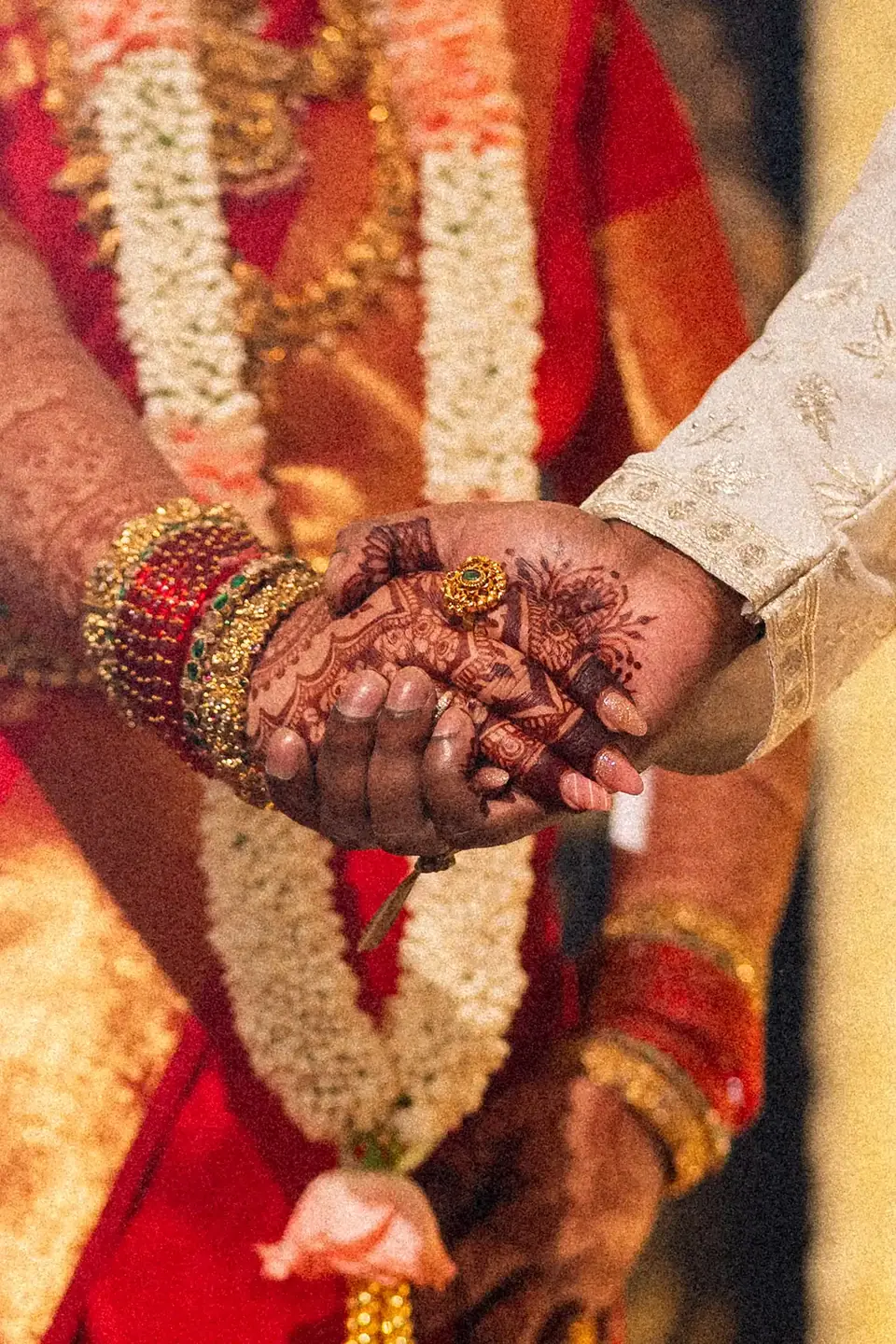 Detail of the couple's joined hands between red silk and jasmine