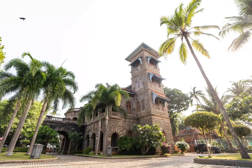 A stone manor with a tower among tall coconut palms under a pale sky