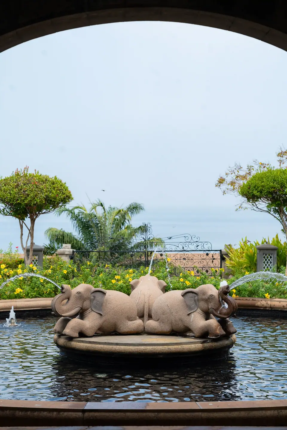 A stone elephant fountain framed by an archway, the sea beyond