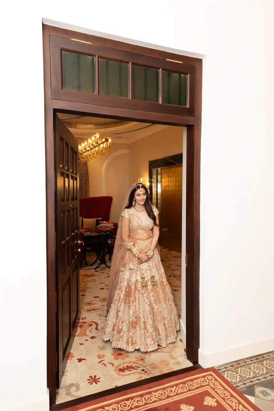 The bride framed in a tall wooden doorway, a red carpet at her feet