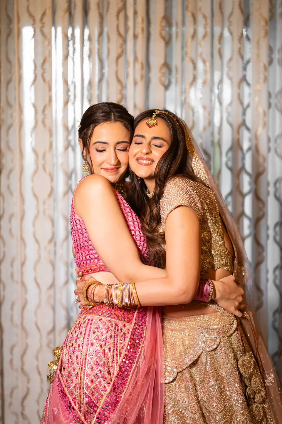 The bride and a friend in pink holding each other close