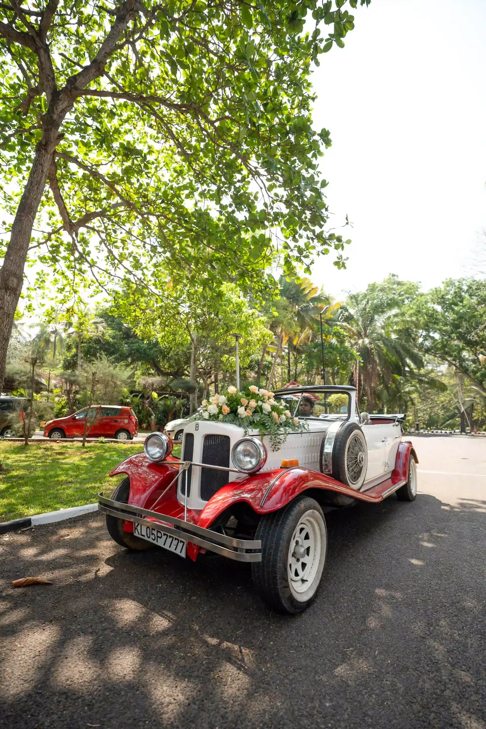 A vintage red and cream open car parked beneath the trees