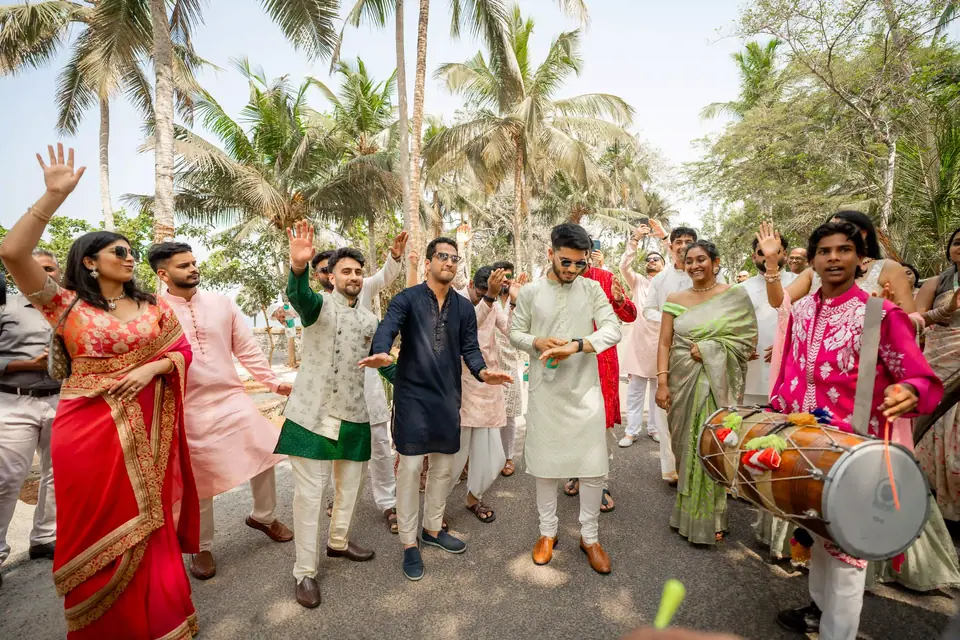 Guests dancing down a palm-lined drive behind a dhol player