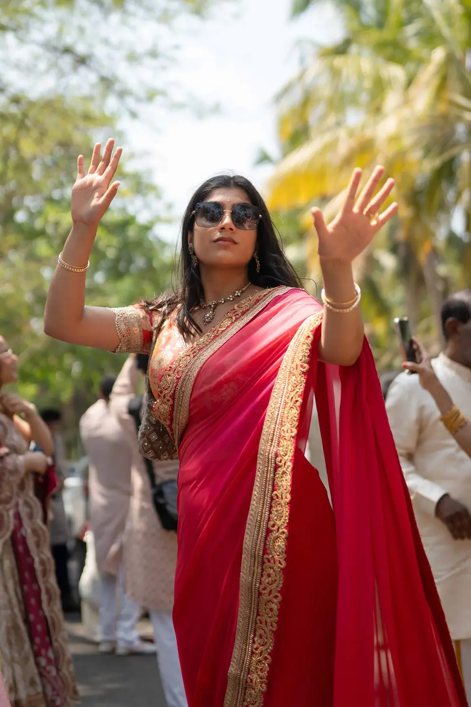 A guest in a red saree dancing with both hands raised