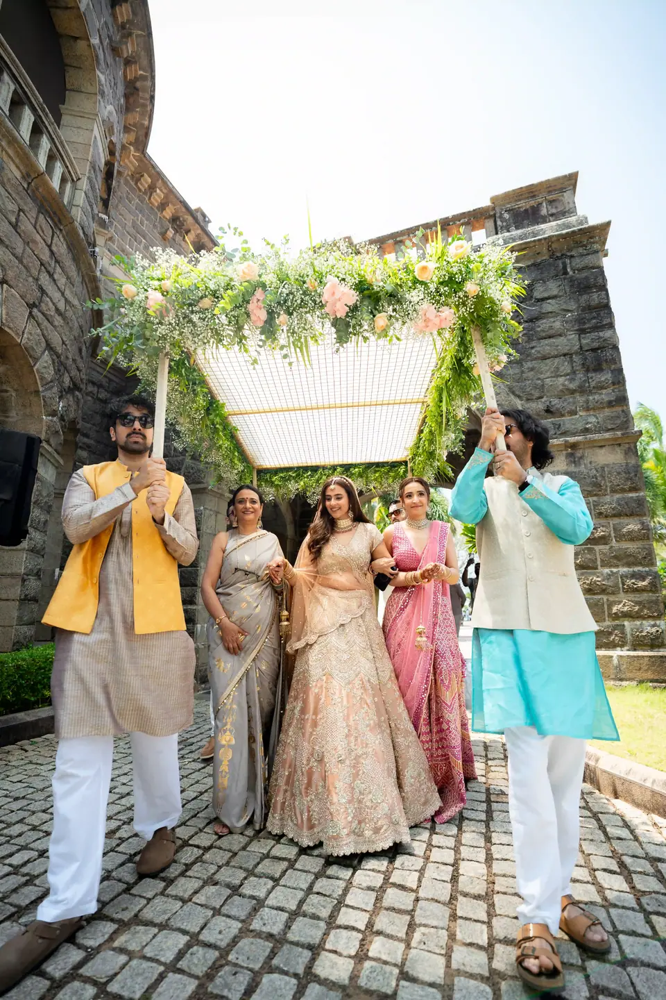 The bride walking under a flowered canopy carried by her brothers