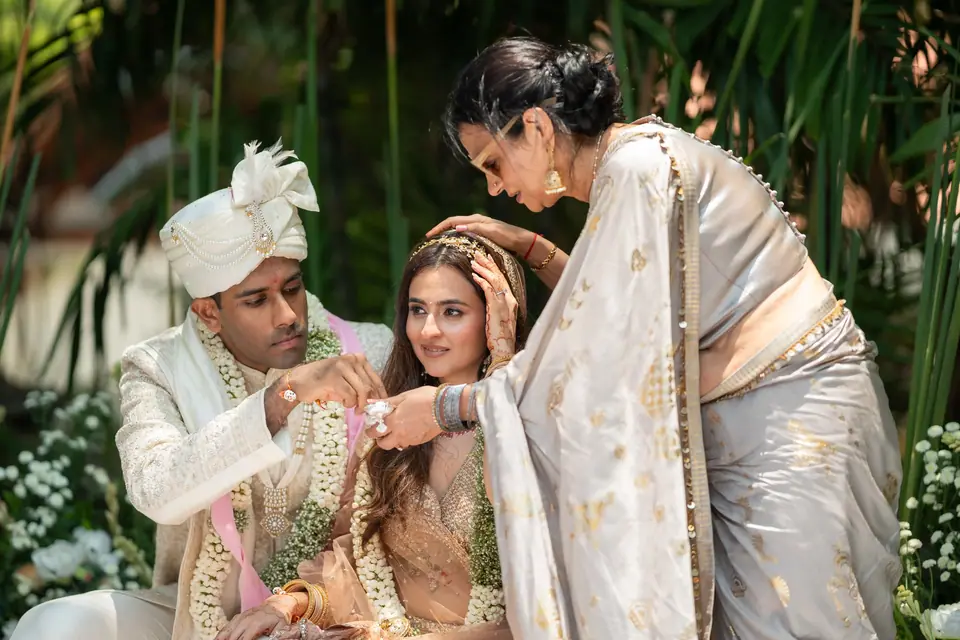 An elder adjusting the bride's hair as the groom looks on