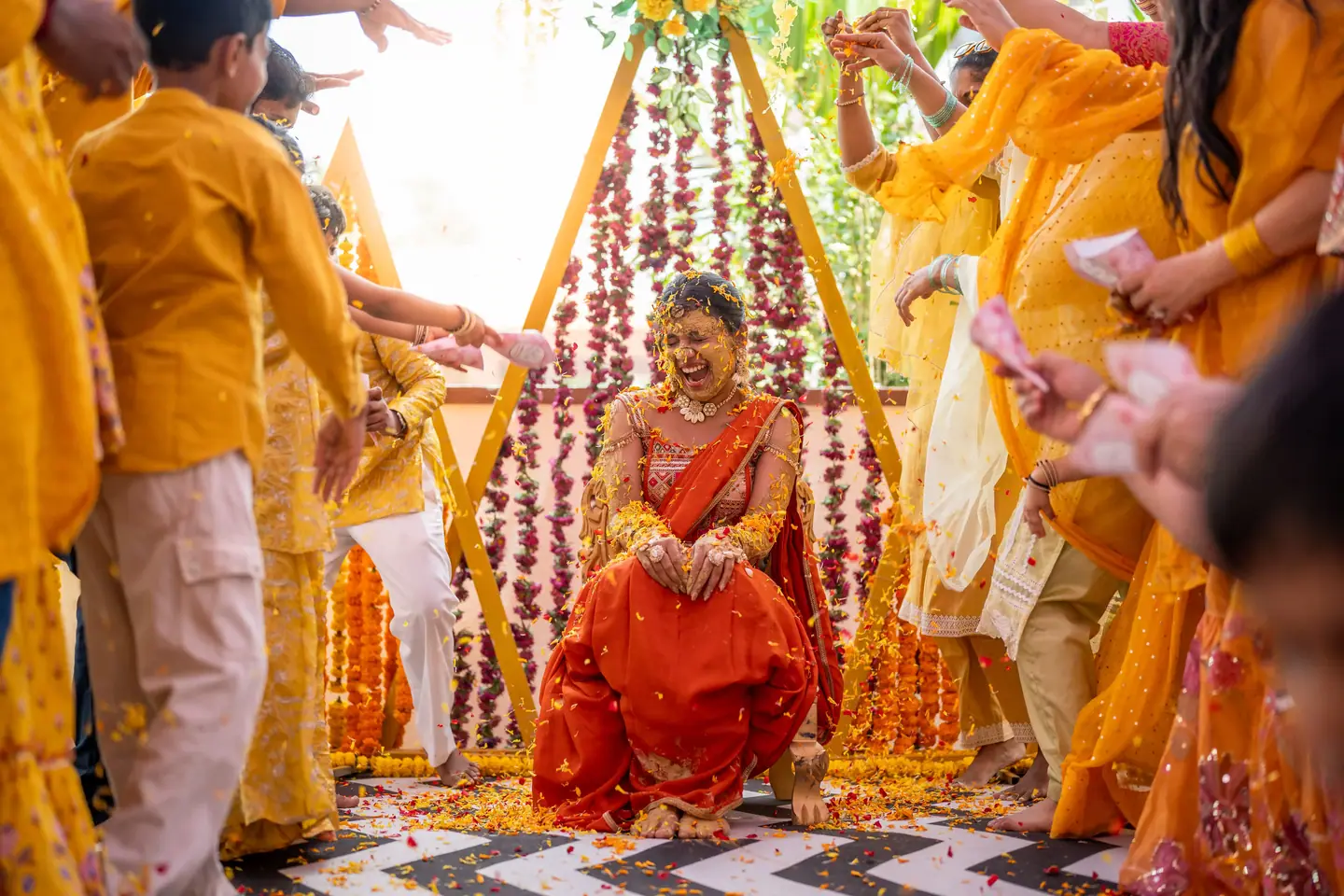 Sahana seated under the haldi mandap as family scatter petals around her