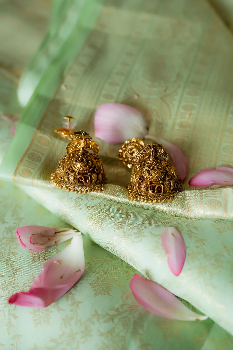 Gold earrings resting on pale green silk with scattered rose petals