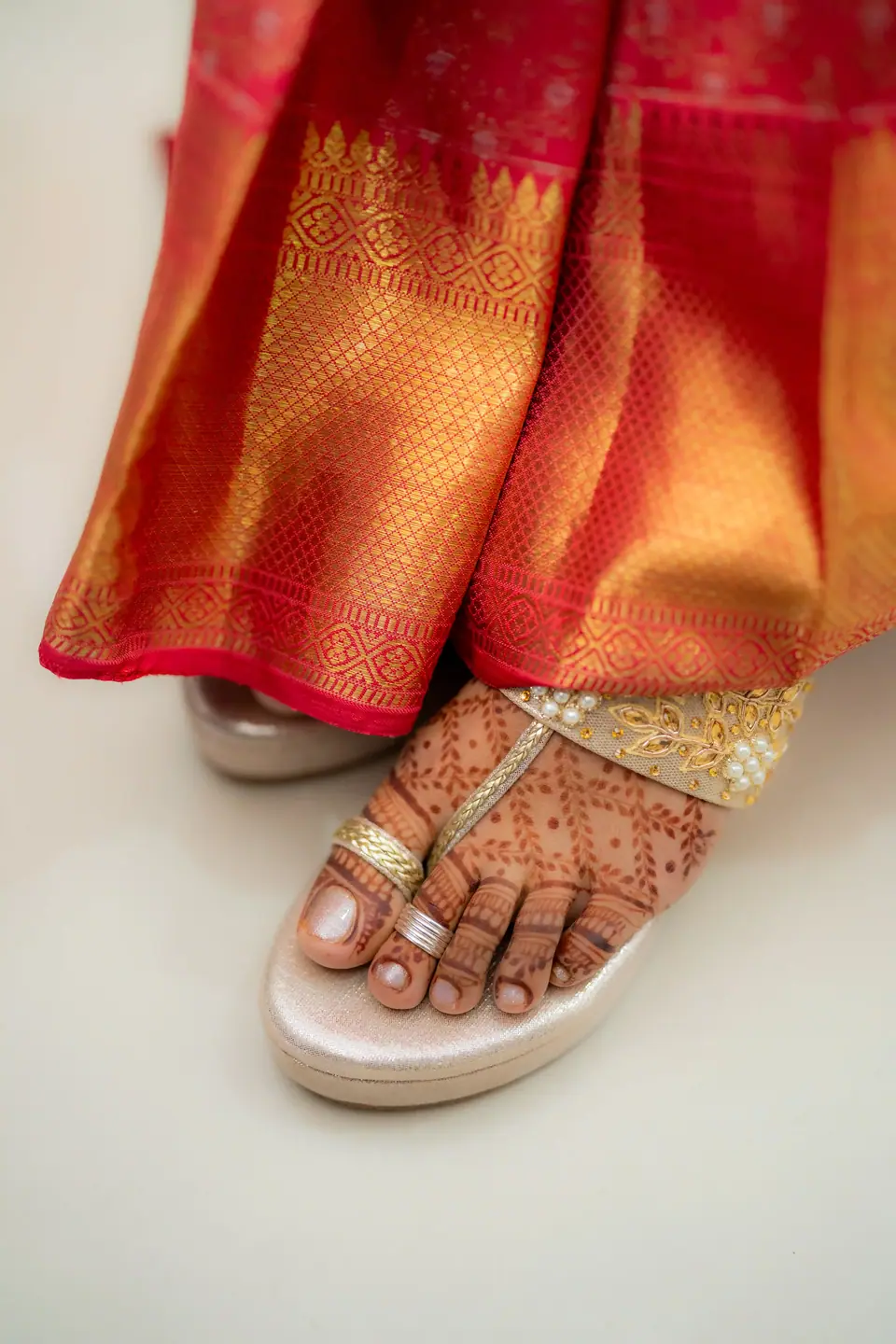 Detail of a hennaed foot in a jewelled sandal beneath red and gold silk