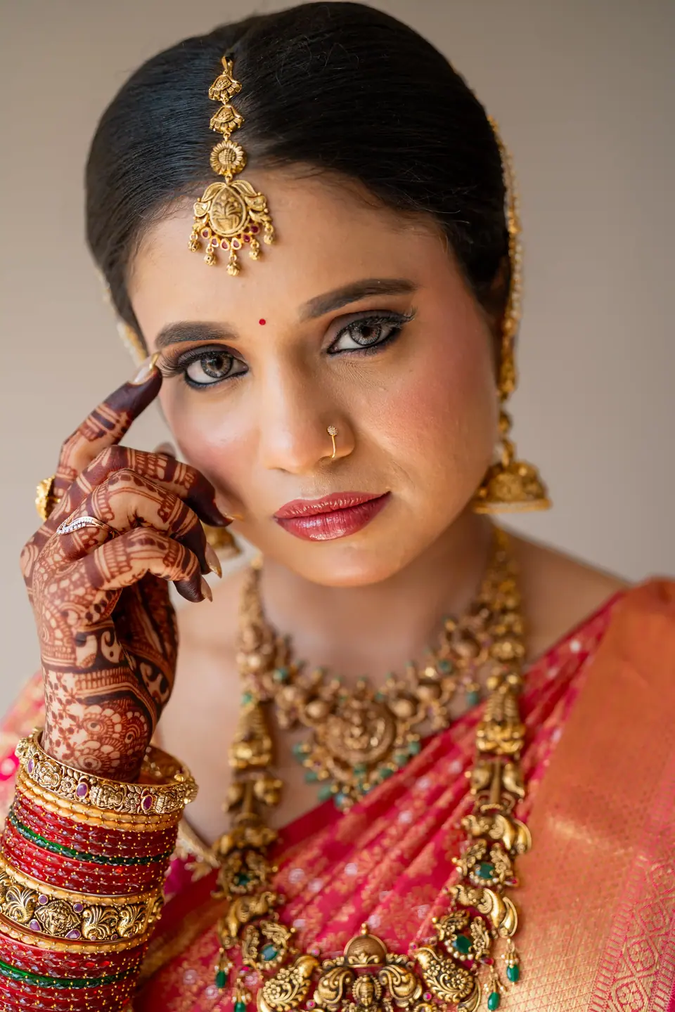 Close portrait of the bride in pink silk and temple jewellery, hand at her cheek