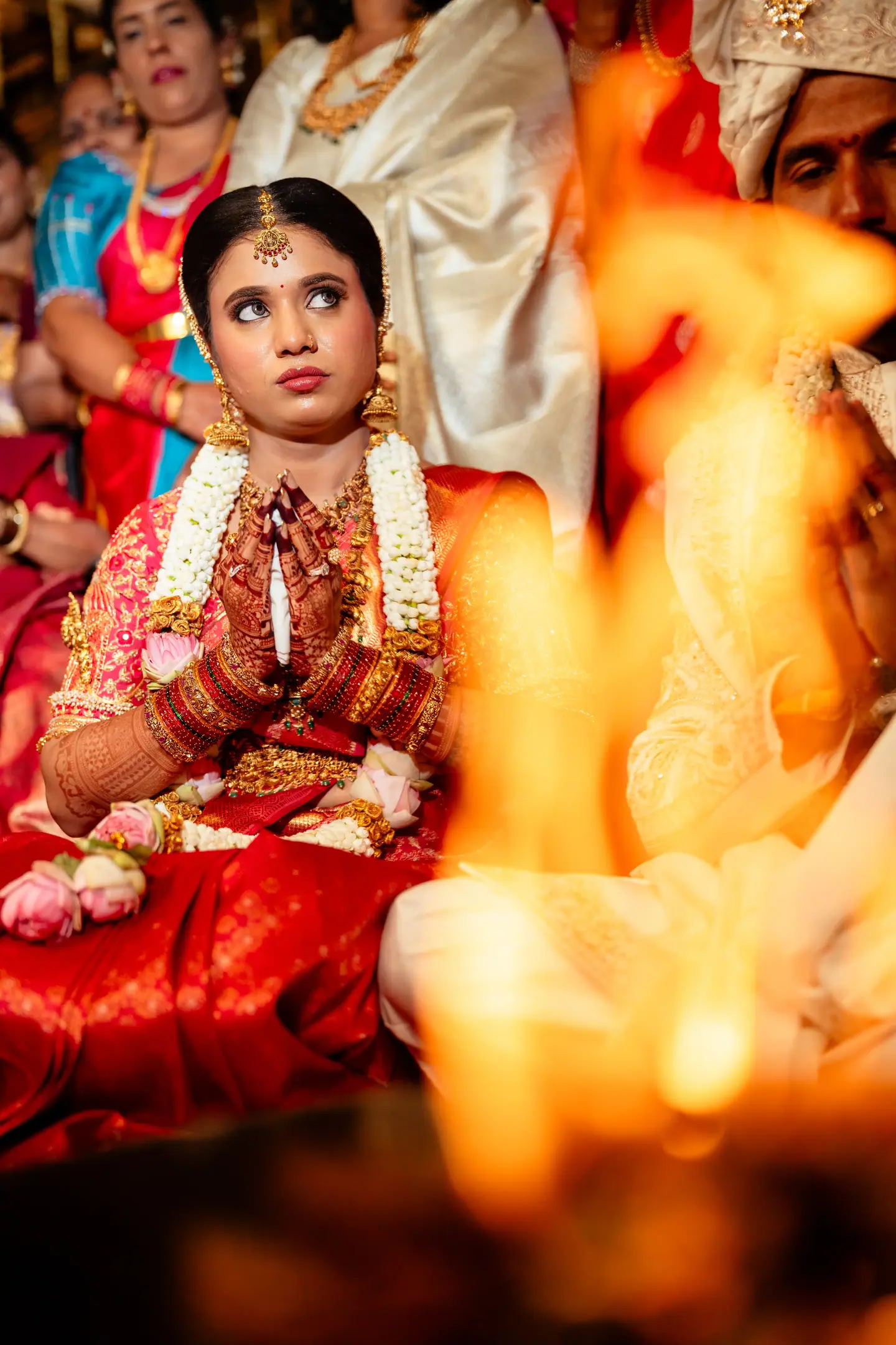 The bride with hands folded, seen through the sacred fire