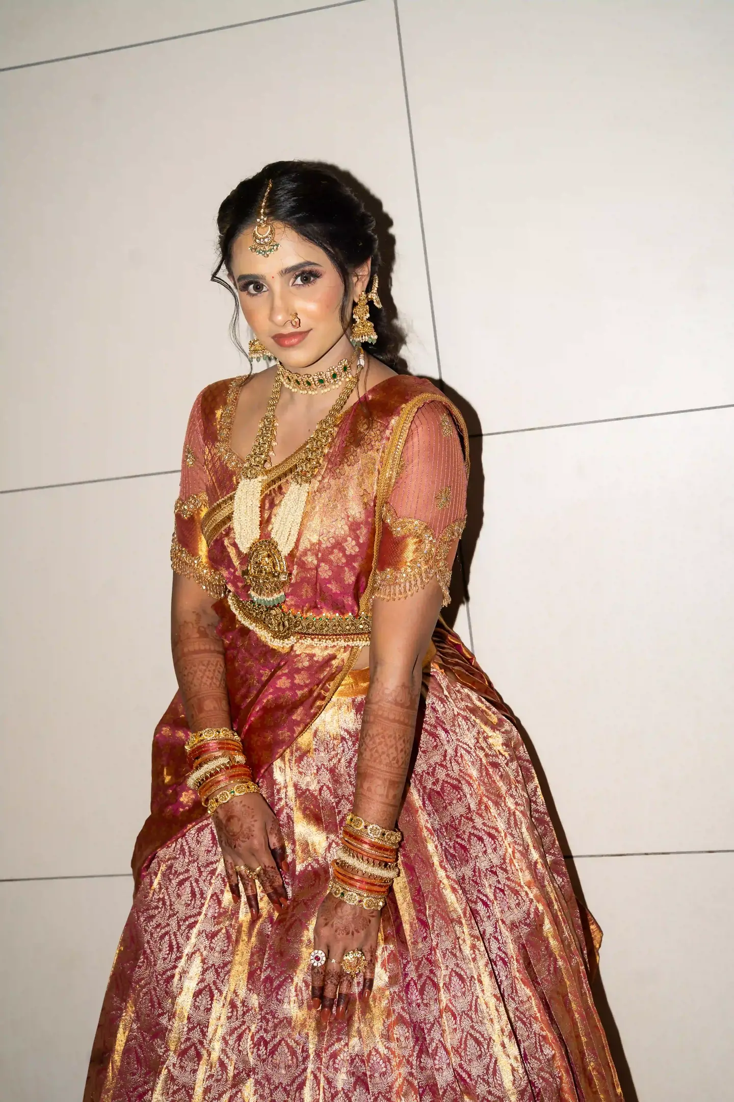 The bride in red and gold silk against a pale tiled wall