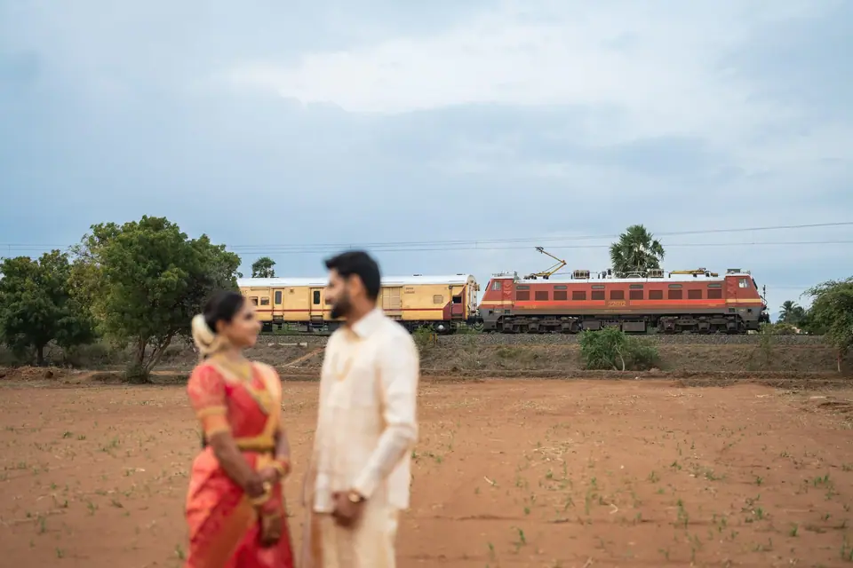 The couple standing in a red-earth field as a train crosses the horizon behind them