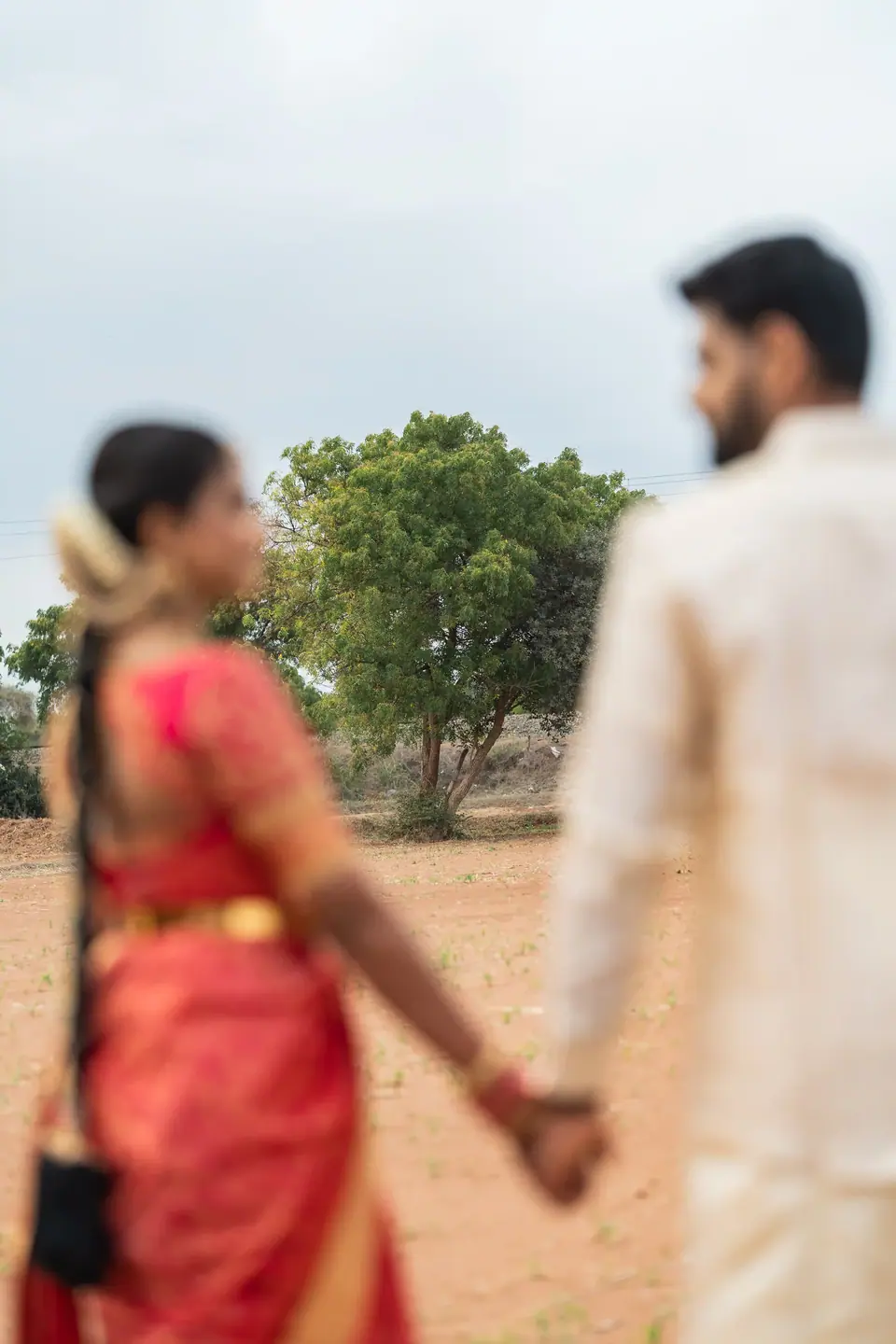 The couple holding hands in the field, the bride soft in the foreground