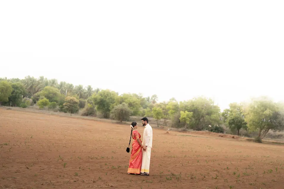 The couple small and far away in a wide, empty field under a white sky