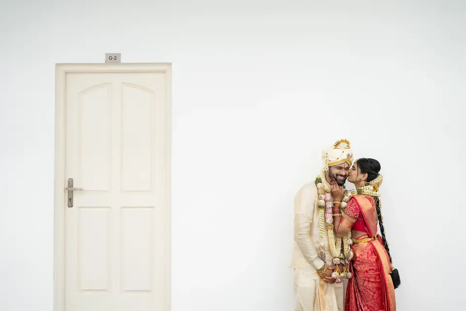 The couple standing against a white wall beside a closed white door