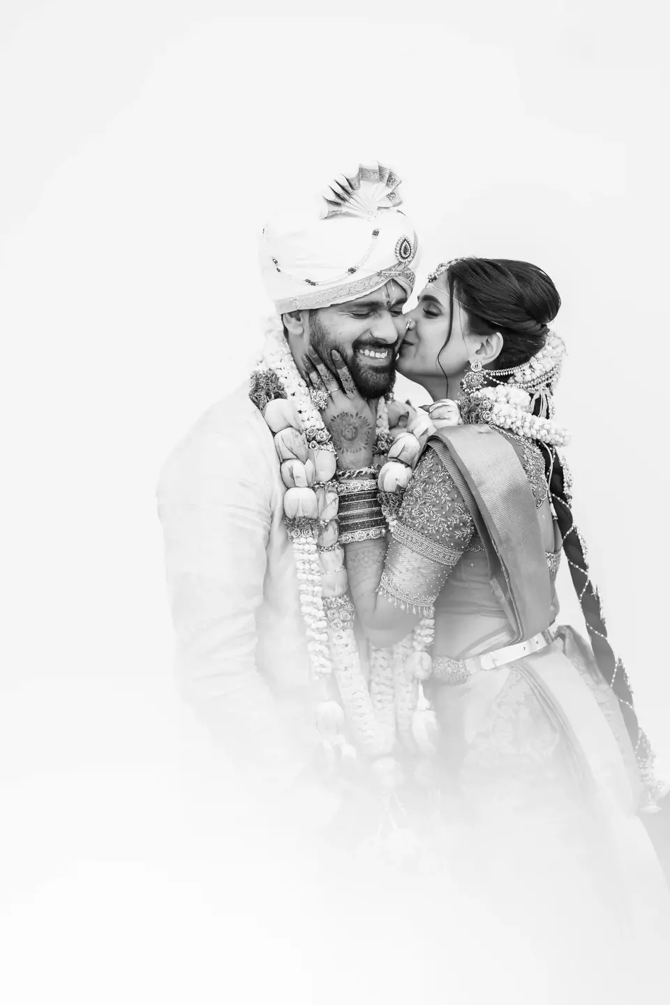Black and white: the bride kissing the groom's cheek in soft high-key light