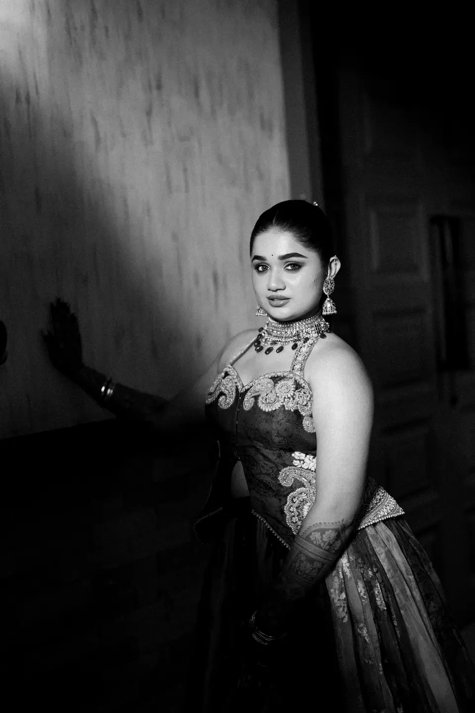 Black and white: the bride leaning on a dark wall, one hand raised against it