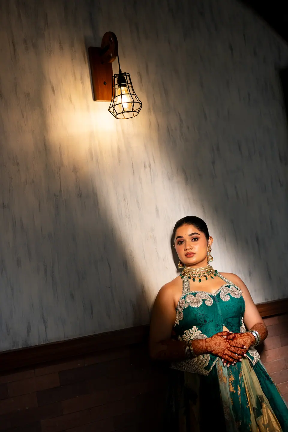 The bride in teal silk beneath a caged wall lamp, a beam of light across the wall
