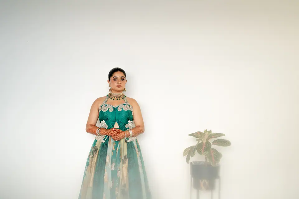 The bride standing small against a bare white wall beside a potted plant