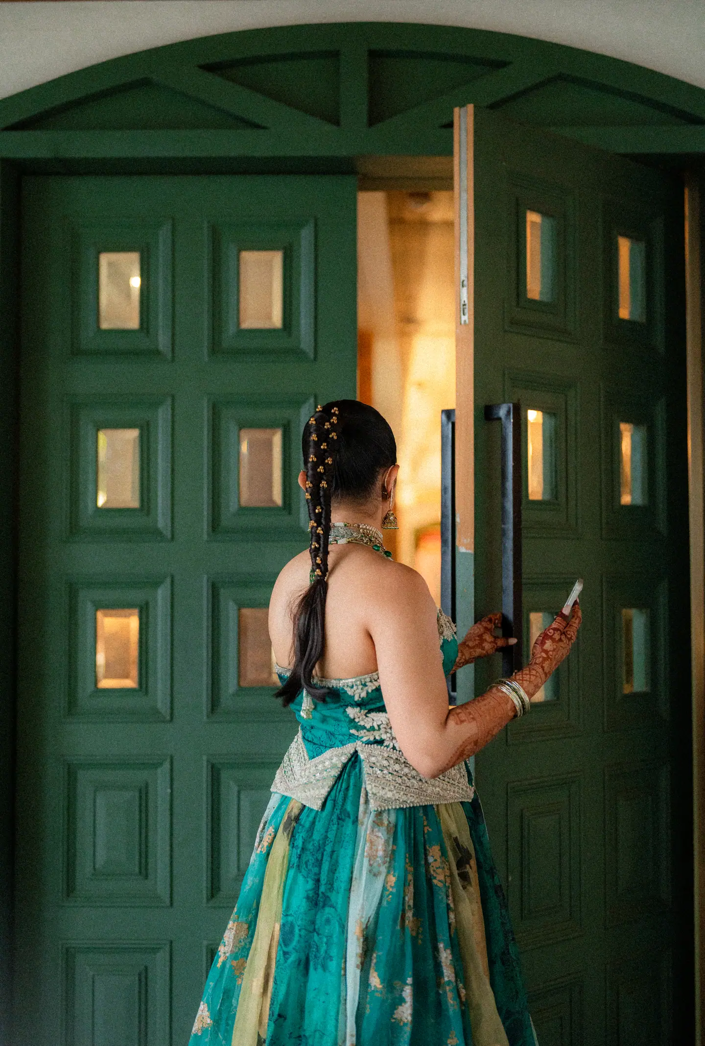 The bride in teal silk reaching for the handle of a tall green door