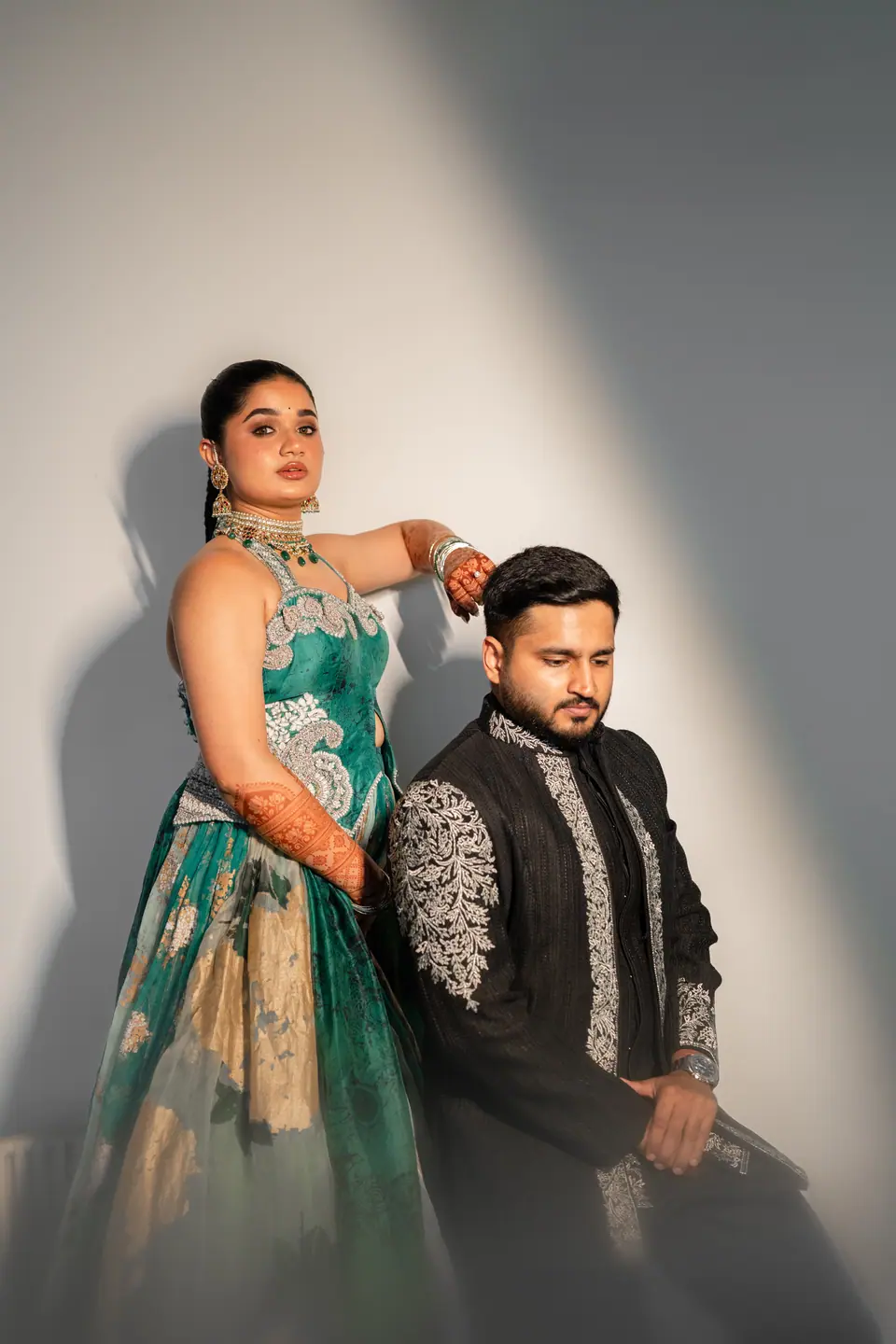 The couple against a white wall, the bride resting her arm on the groom's shoulder