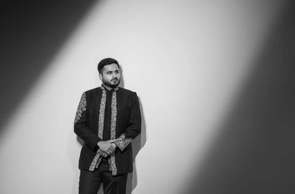 Black and white: the groom in an embroidered jacket standing in a diagonal shaft of light
