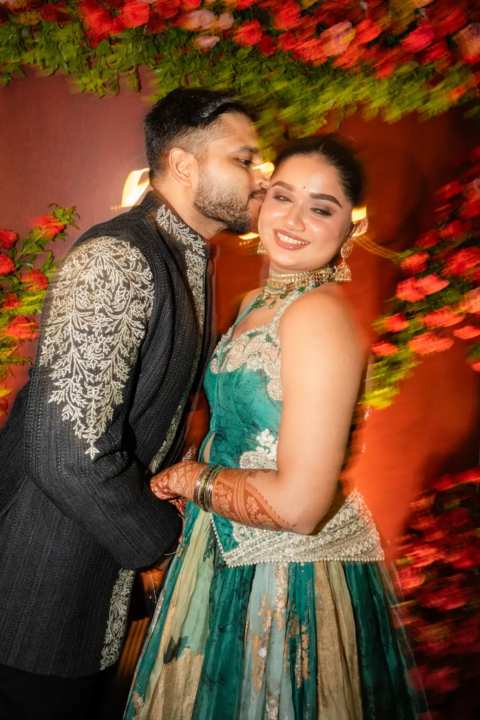 The groom kissing the bride's cheek in front of the rose wall