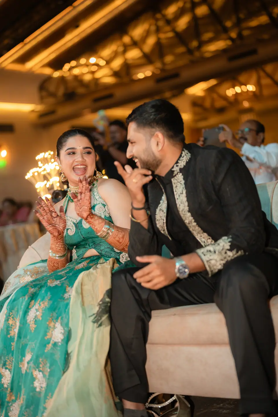 The bride laughing as the groom leans in to say something, both watching the stage