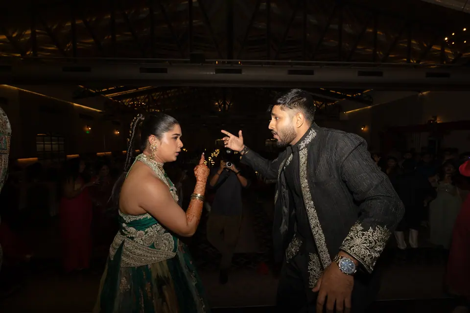 The couple facing each other on a dark dance floor, mid-step