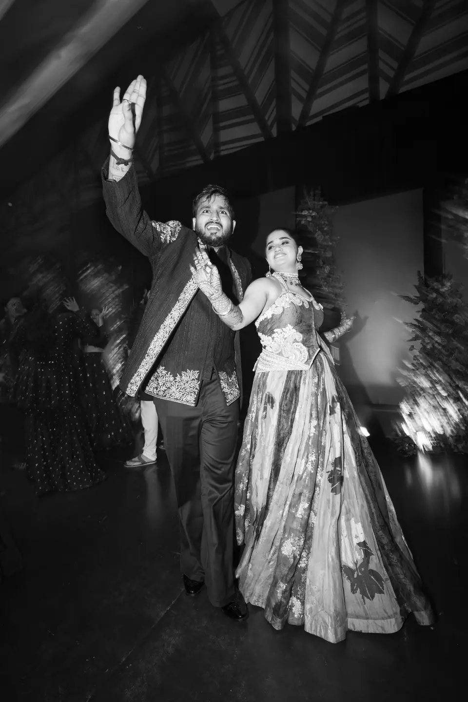 Black and white: the groom with one arm raised, leading the bride across the floor