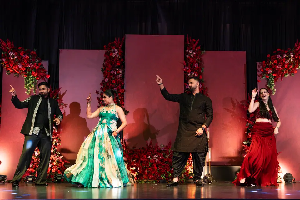 The couple and their friends dancing on stage before a wall of red roses